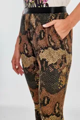 Pantalón tipo babucha con estampado de piel de serpiente en tonos marrones y naranjas, con cintura elástica negra.