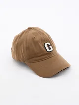 Gorra tipo baseball color beige con letra G bordada en el frente en color blanco con contorno negro.