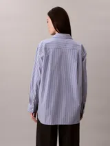 Camisa Calvin Klein de corte regular, con diseño de rayas verticales en tonos azul y blanco. Cuenta con cuello camisero, cierre frontal de botones, mangas largas y un bolsillo aplicado en el pecho con el logo bordado de la marca.