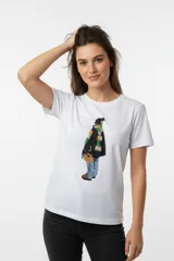 Remera de algodón blanca de corte ajustado, con cuello redondo a la base y mangas cortas. Presenta un estampado central con detalles en glitter que ilustra una figura humana de espaldas con bufanda colorida.