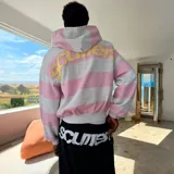Campera con capucha de corte boxy, con diseño de rayas horizontales en tonos gris melange y rosado. Presenta la inscripción bordada en relieve de la marca en la espalda en tono amarillo pastel.
