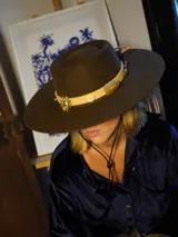 Sombrero de fieltro color marrón con ala ancha y cinta de cuero con apliques metálicos.