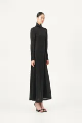 Vestido largo negro de manga larga y cuello tortuga, con silueta ajustada en el torso y falda amplia con aberturas laterales. El tejido presenta un brillo sutil.