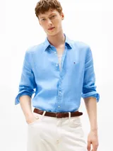 Camisa de manga larga color celeste, confeccionada en lino con un acabado pigmentado. Presenta cuello clásico, cierre frontal de botones y el logo de Tommy Hilfiger bordado en el pecho.