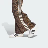 Pantalón Adidas Originals de pierna ancha, confeccionado en satén con estampado animal print de leopardo. Cuenta con cintura elástica, las clásicas tres tiras blancas en los laterales y el logo del trifolio bordado en el frente.