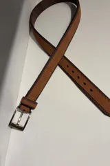 Cinturón de cuero de carpincho en color suela, con textura granulada característica, bordes pespunteados en cuero oscuro y hebilla metálica en tono bronce envejecido.