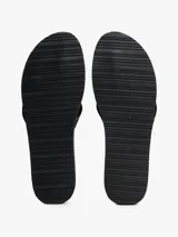 Ojotas negras con tiras de textil trenzado que presentan el logo de Tommy Hilfiger en jacquard con detalles en blanco y dorado. La suela es de EVA dentada con una entresuela a contraste blanca.