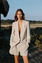 Shorts color beige confeccionados en hilatura con lino, de tiro alto. Presentan bolsillos delanteros, falsos bolsillos traseros con solapa y pinzas delanteras. Cierre frontal con cremallera y gancho metálico.