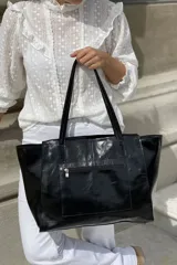 Bolso tipo shopper de gran tamaño confeccionado en cuero vacuno color marrón oscuro. Presenta laterales con textura grabada tipo cocodrilo y detalles de costuras decorativas con tientos de cuero en los paneles frontales y traseros. Incluye doble asa de hombro, cierre superior y placa metálica decorativa en el frente.