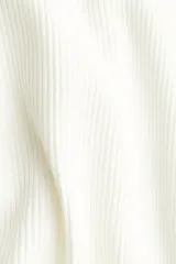 Top corto de punto acanalado color blanco, con escote amplio que deja los hombros al descubierto y leve escote en V. Mangas largas acampanadas con ribete de volados en puños y bajo.