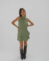 Vestido corto color verde militar con cuello halter alto, sin mangas y falda con volados superpuestos.