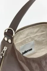 Bolso tipo hobo de diseño media luna, confeccionado en cuero caprino con acabado charol y textura grabada. Cuenta con cierre superior de cremallera, asa ajustable y el logo de la marca en la parte frontal.