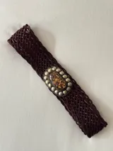Cinto trenzado de cuero color chocolate con hebilla ovalada de metal envejecido, decorada con una piedra central jaspeada y tachas metálicas alrededor.