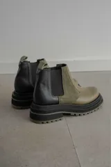 Botines Chelsea de cuero color verde oliva y negro, con elásticos laterales negros, tirador trasero y suela track de goma color verde oliva.