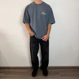 Remera negra de corte oversize con estampa gráfica en la espalda que presenta un oso con anteojos y bandana, acompañada de la frase 'Richer, Louder & Unbothered Than Ever'.