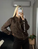 Campera tipo bomber confeccionada en gamuza, con cierre frontal metálico y detalle de flores bordadas en relieve en el frente.