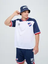 Remera de fútbol Umbro del Club Nacional de Football, de diseño tricolor con cuerpo azul marino, mangas y canesú rojos, y cuello en V con detalles en blanco y azul. Incluye el logo de Umbro en el pecho derecho y el escudo del club en el izquierdo.