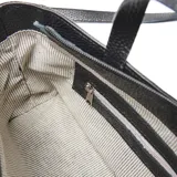 Bandolera de cuero con textura granulada, cuenta con doble asa de mano y correa larga ajustable y extraíble. Presenta un bolsillo frontal con cierre y placa metálica con logo de la marca en el centro.