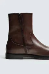 Bota de caña media fabricada en piel color marrón oscuro, con cierre de cremallera lateral, horma cuadrada y suela con ligero tacón.