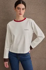 Remera de manga larga color blanco con cuello redondo en color rojo y puños en color marrón. Presenta el logo de la marca bordado en el pecho.