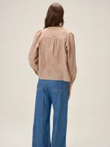 Camisa de color crema con bordados florales, cuello mao, cierre frontal con botones y mangas largas abullonadas con volados en los hombros.