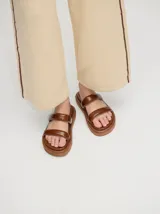 Sandalias de cuero vacuno color marrón con acabado brillante, diseño de dos tiras anchas acolchadas y plataforma baja.