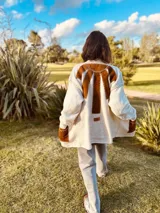 Tapado tejido en lana color crema con apliques de cuero marrón en la espalda y bolsillos delanteros. Presenta un diseño de corte largo y holgado con costuras visibles que unen los materiales.