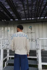 Buzo de punto trenzado en color crema, con cuello redondo y la palabra 'URUGUAY' estampada en letras azules en la parte superior de la espalda.