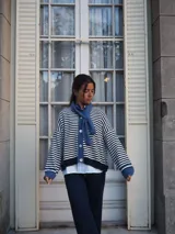 Sweater de punto a rayas horizontales blancas y azul marino, con cuello redondo, cierre frontal con botones y mangas largas con puños y detalles en tono azul.