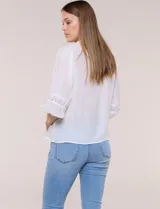 Blusa blanca de manga larga con escote en V y detalles de encaje en la botonera frontal, cuello y puños.