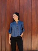 Camisa de jean azul con cuello mao, cierre frontal con botones rojos y mangas tres cuartos abullonadas con puños elásticos.