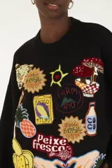 Buzo de punto negro, de corte holgado, con cuello redondo y mangas largas con puños ajustados. Presenta múltiples apliques bordados con motivos tropicales y coloridos en la parte frontal.