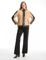 Campera de corderito sintético color beige con paneles y detalles en cuero sintético negro. Presenta cuello alto con tira y hebilla metálica, cierre frontal metálico y mangas largas con paneles de cuero sintético.