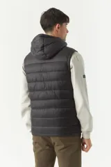 Chaleco negro acolchado con capucha ajustable, cierre frontal y bolsillos laterales con cierre. Logo de la marca en el pecho. Colección Otoño Invierno 2025. El modelo usa talle M. Composición 100% nylon.