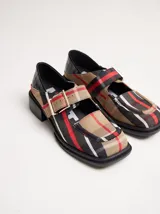 Zapatos tipo guillermina con punta cuadrada, confeccionados en lona resistente con estampado de cuadros escoceses en tonos beige, rojo y negro. Presentan una correa ajustable con hebilla metálica color bronce y una suela con taco de 4 cm.