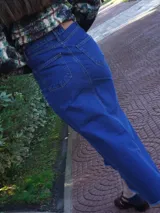 Pollera larga de denim azul de tiro medio, con diseño de corte evasé y terminación desmechada en el ruedo. Cuenta con abertura lateral y detalle de parche de cuero.