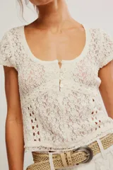 Remera de encaje calado color blanco, con calce ajustado, escote redondo amplio, botonadura corta en el frente y mangas cortas.