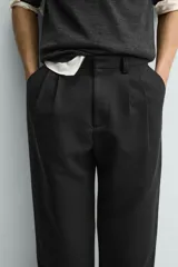 Pantalón de corte wide fit confeccionado en tejido con mezcla de lyocell. Presenta pliegues frontales dobles, bolsillos laterales y bolsillos traseros de vivo. Cierre frontal con cremallera y gancho metálico oculto.