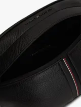 Riñonera Tommy Hilfiger de estilo urbano, color negro, confeccionada en mezcla de algodón y poliéster. Cuenta con correa ajustable con broche, compartimento principal con cierre, detalle de franja tricolor central y logo metalizado de la marca.