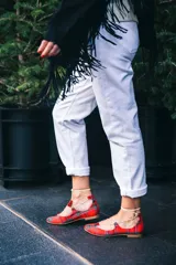 Bailarinas rojas con estampado tartán, anudadas al tobillo con cordones blancos y borlas decorativas.