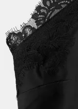 Vestido largo lencero de satén negro, con cuello halter, tirantes finos, detalles de encaje en el escote y en el bajo asimétrico.