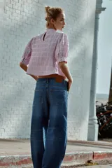 Camisa rosa de cuello alto, mangas cortas abullonadas y detalles de encaje y entredós en el frente y las mangas.