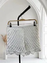 Short de tejido de punto calado color blanco, con forro interior. Presenta un patrón de rayas diagonales y un ruedo con borde festoneado.