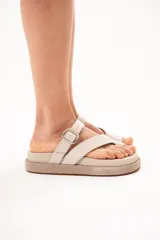 Sandalias de cuero color arena, con diseño de tiras cruzadas, sujetador para el dedo y hebilla metálica lateral. Cuenta con suela acolchada y plataforma plana forrada.