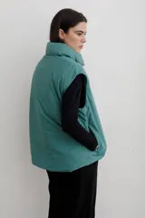 Chaleco puffer con cuello alto y cierre frontal oculto, estampado con diseño floral y de aves en tonos rojos sobre base azul oscuro.
