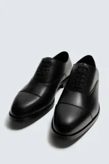 Zapato de vestir tipo Oxford en color negro, con diseño de puntera reforzada y cierre mediante cordones. Presenta una silueta clásica y elegante con tacón bajo.