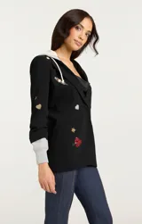 Blazer negro con capucha gris, solapas con muescas, cierre con botones y bolsillos con solapa en la parte delantera. Decorado con parches bordados de corazones, estrellas y otros motivos.