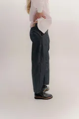 Pantalón de denim oscuro con tiro bajo y calce relajado. Presenta un cierre frontal con botones a la vista y costuras en contraste.