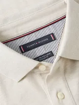 Chomba de corte regular color beige claro, con cuello tipo chomba, cartera de dos botones y logo de Tommy Hilfiger bordado en el pecho. Diseño de rayas en el interior del cuello.