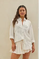 Camisa beige de manga larga con bordados florales plateados y lentejuelas, cuello clásico y cierre frontal de botones.
